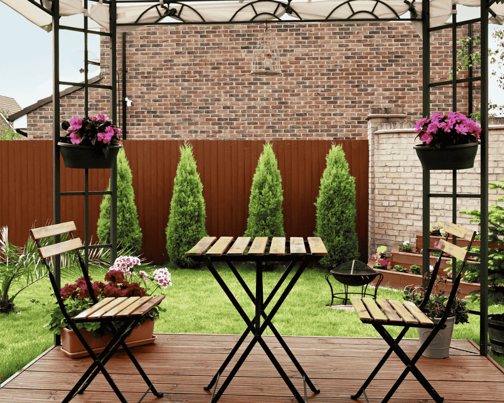 Garden Decking with Gazebo and Seating Area Stylish wooden decking with wicker chairs and table under a white gazebo, surrounded by lush garden flowers and lawn – perfect for outdoor relaxation and garden design inspiration.